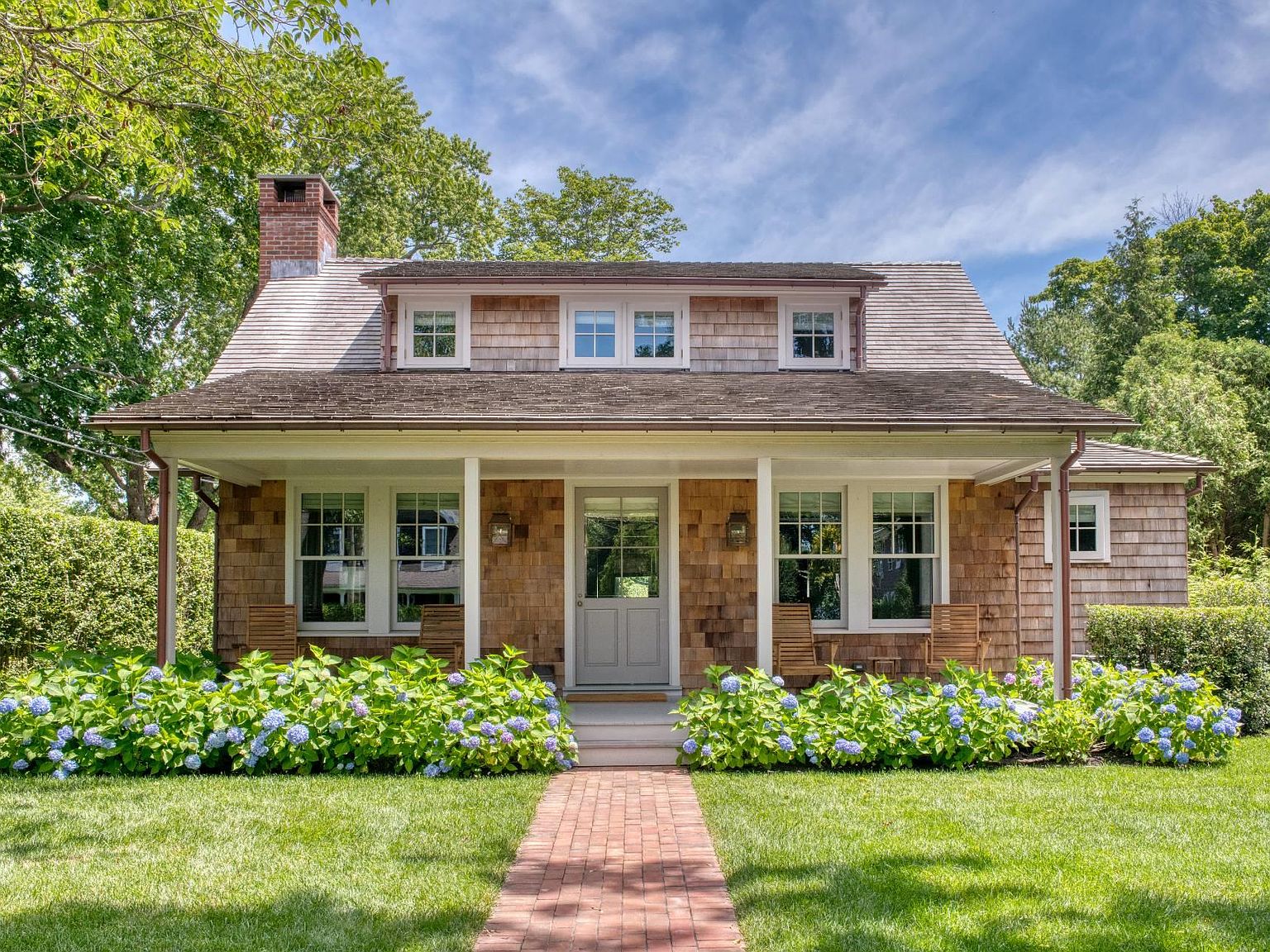 Cedar-shingle home with a white-trimmed porch and blue hydrangeas